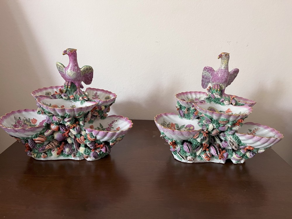 A pair of 18th-century First Period Worcester soft-paste porcelain tiered centrepieces featuring moulded shell dishes, encrusted marine decoration, and bird finials in pink and green enamels.