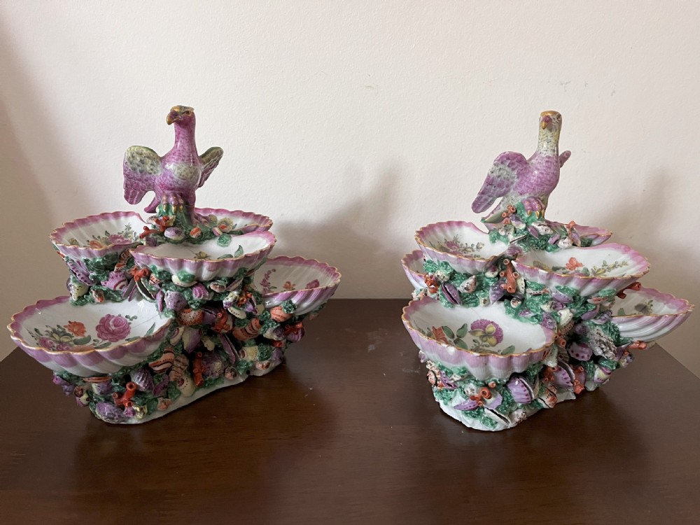 A pair of 18th-century First Period Worcester soft-paste porcelain tiered centrepieces featuring moulded shell dishes, encrusted marine decoration, and bird finials in pink and green enamels. View X