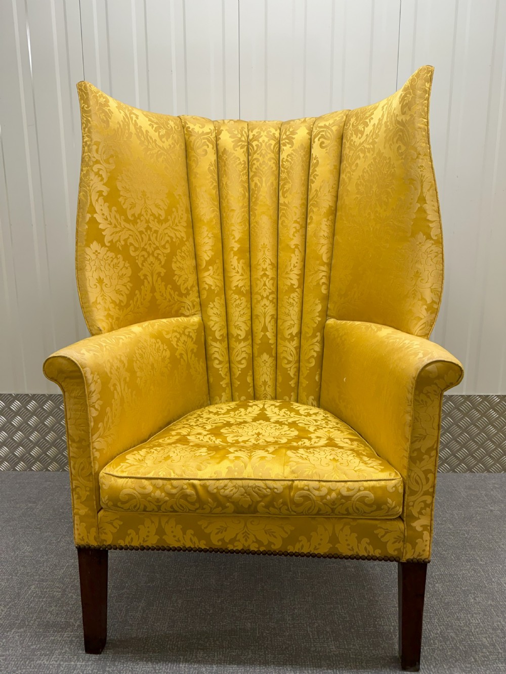 A Georgian mahogany wingback armchair featuring yellow damask patterned upholstery, a channel-fluted backrest, and straight dark wood legs.