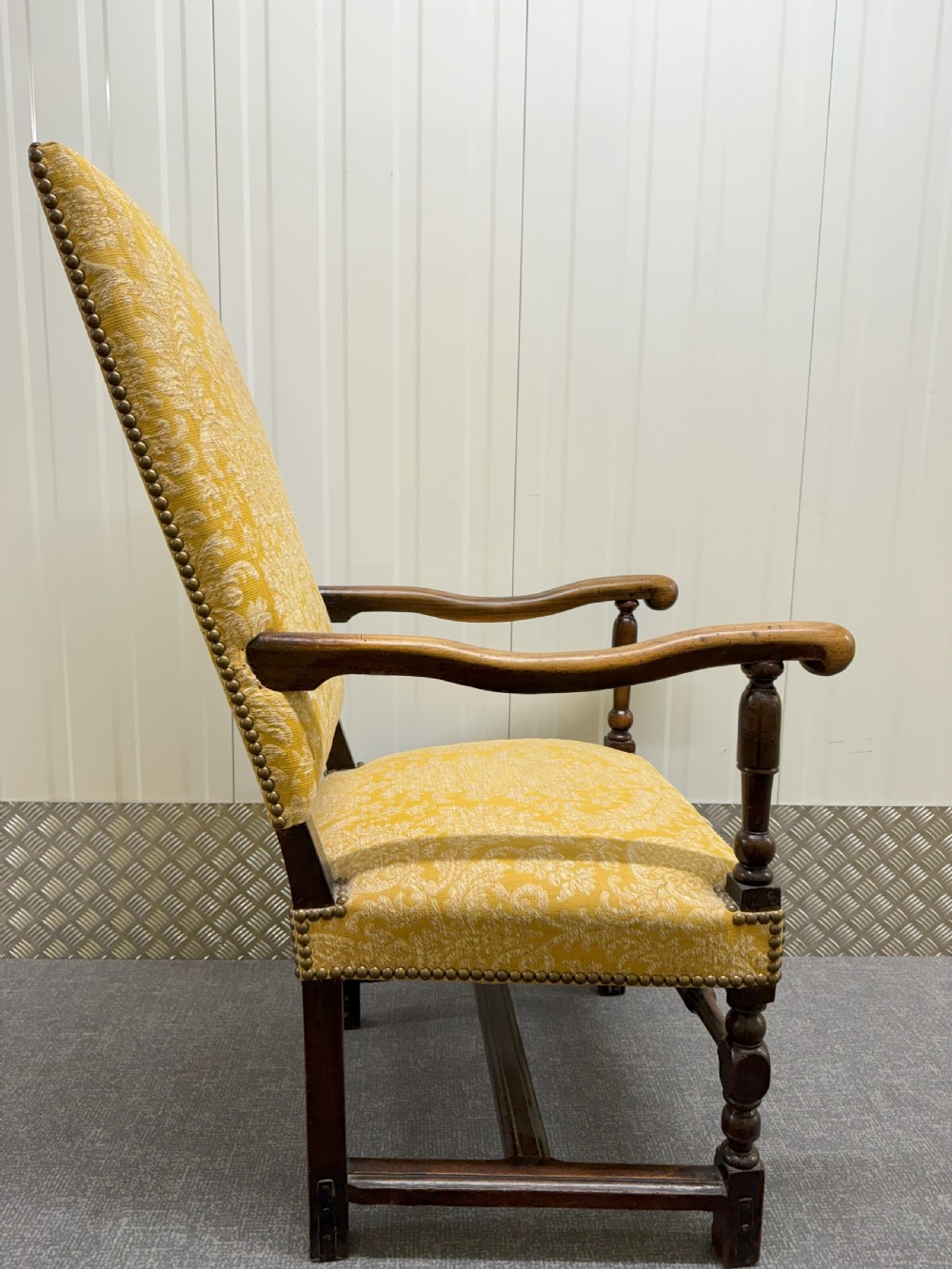 An antique Charles II style walnut elbow chair featuring turned wood legs, scrolled armrests, brass stud details, and yellow damask upholstery. View V