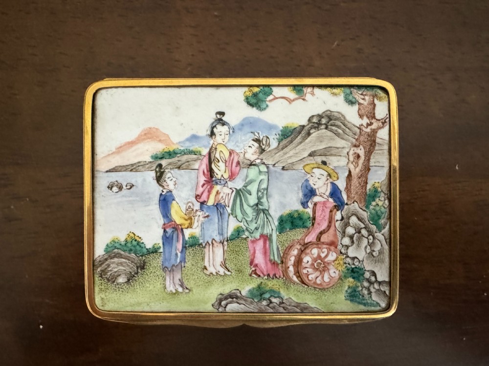 A rectangular 18th-century Chinese Beijing enamel snuff box decorated with a hand-painted scene of figures in traditional attire beside a river and framed by gilded metal.
