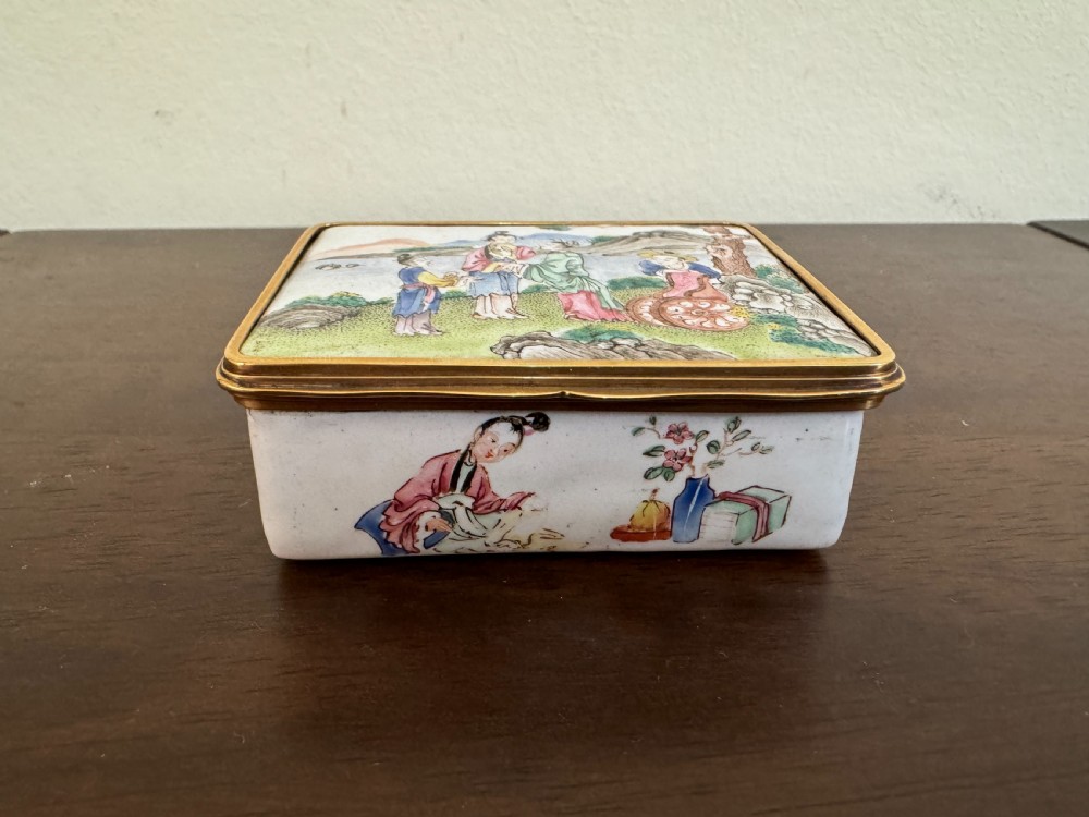 A rectangular 18th-century Chinese Beijing enamel snuff box decorated with a hand-painted scene of figures in traditional attire beside a river and framed by gilded metal. View II