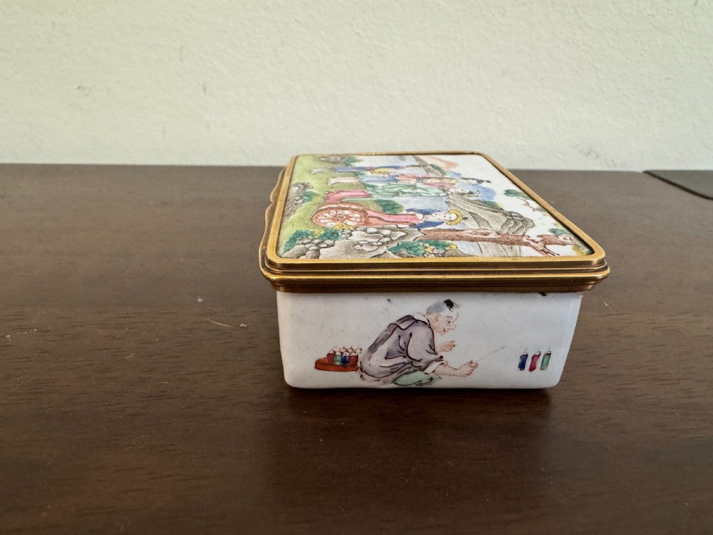 A rectangular 18th-century Chinese Beijing enamel snuff box decorated with a hand-painted scene of figures in traditional attire beside a river and framed by gilded metal. View III