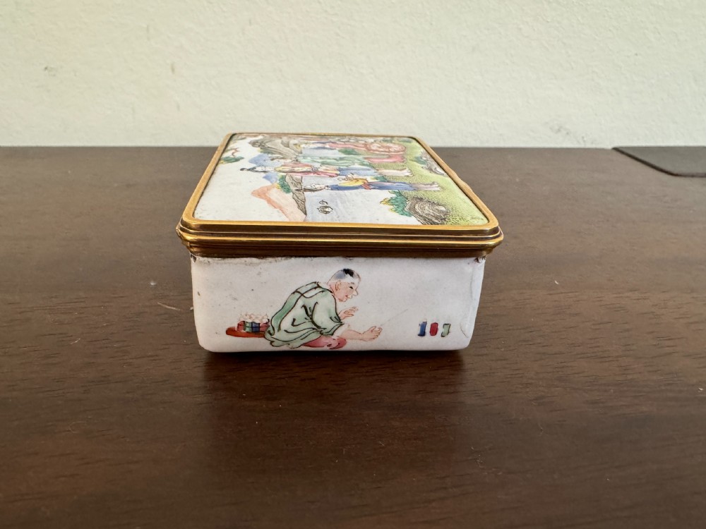 A rectangular 18th-century Chinese Beijing enamel snuff box decorated with a hand-painted scene of figures in traditional attire beside a river and framed by gilded metal. View V