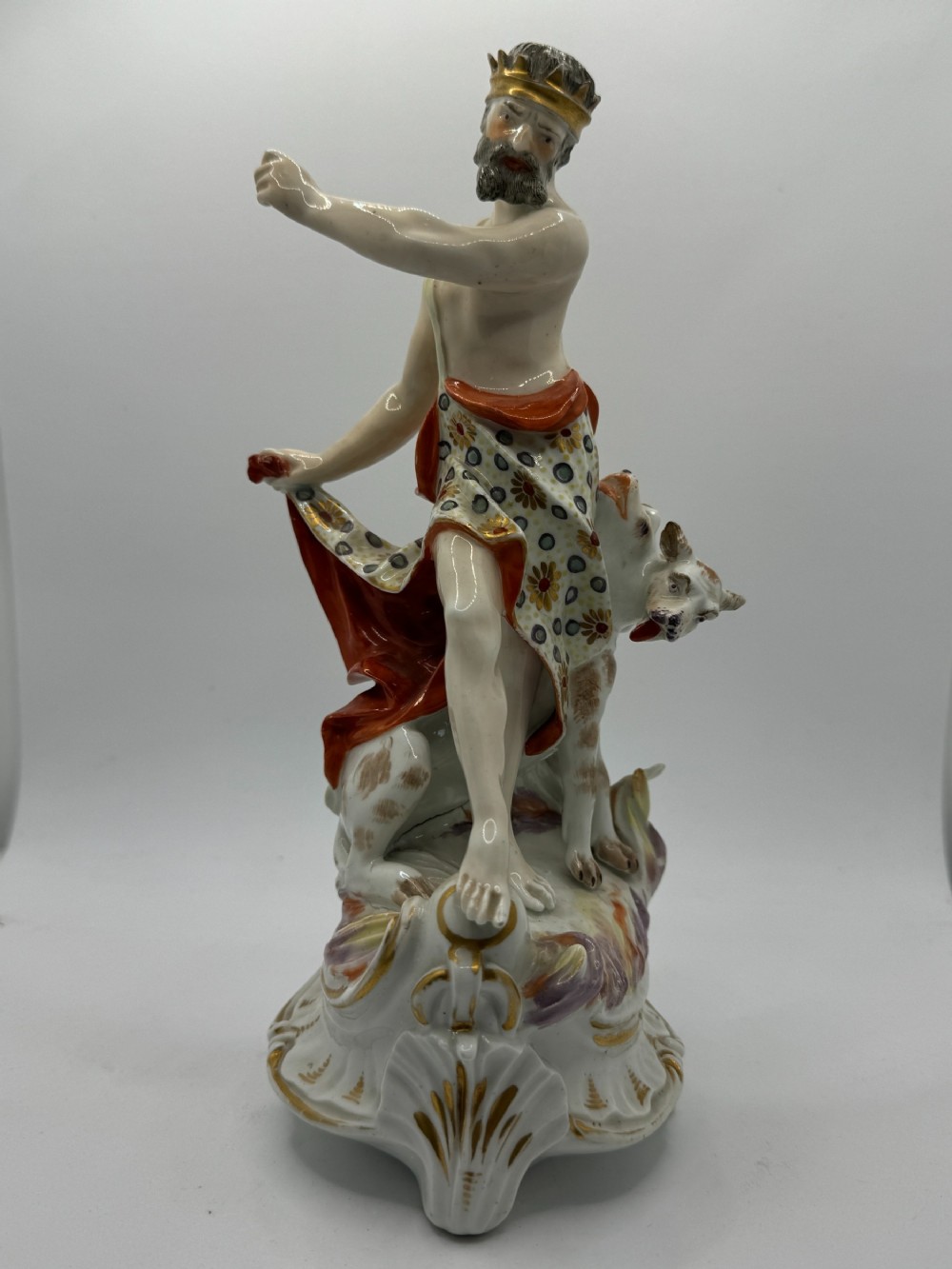 An 18th-century Derby porcelain figure group depicting the classical deity Pluto standing with a crown and patterned cloak beside the three-headed dog Cerberus on a scroll base.
