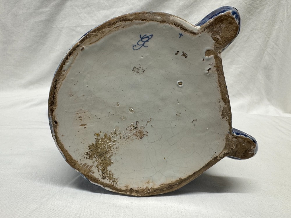 A 19th-century Dutch Delftware ceramic Toby jug shaped as a seated man, decorated with hand-painted blue floral patterns against a white background. View IX