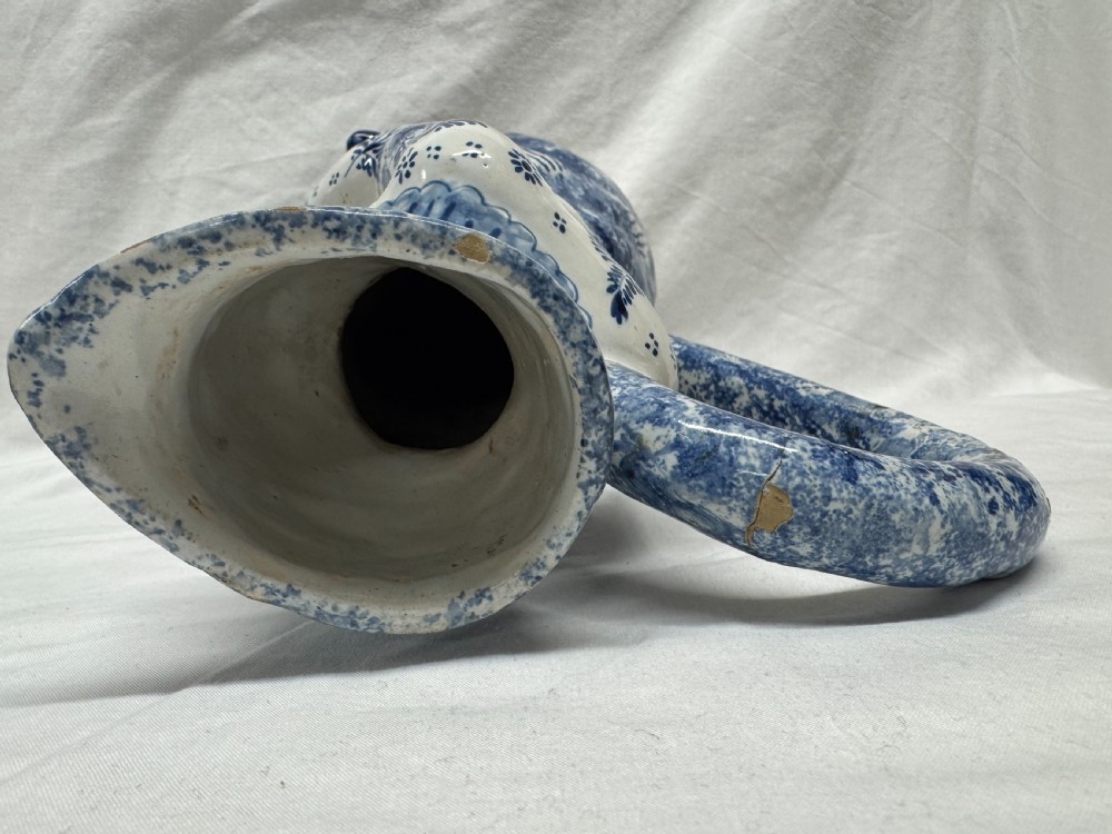 A 19th-century Dutch Delftware ceramic Toby jug shaped as a seated man, decorated with hand-painted blue floral patterns against a white background. View X