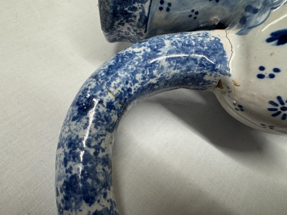 A 19th-century Dutch Delftware ceramic Toby jug shaped as a seated man, decorated with hand-painted blue floral patterns against a white background. View XI