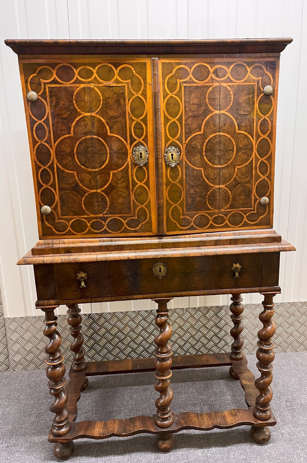 A William & Mary walnut cabinet on stand featuring door panels decorated with geometric oyster veneer stringing, resting on six barley-twist legs with a shaped stretcher base.