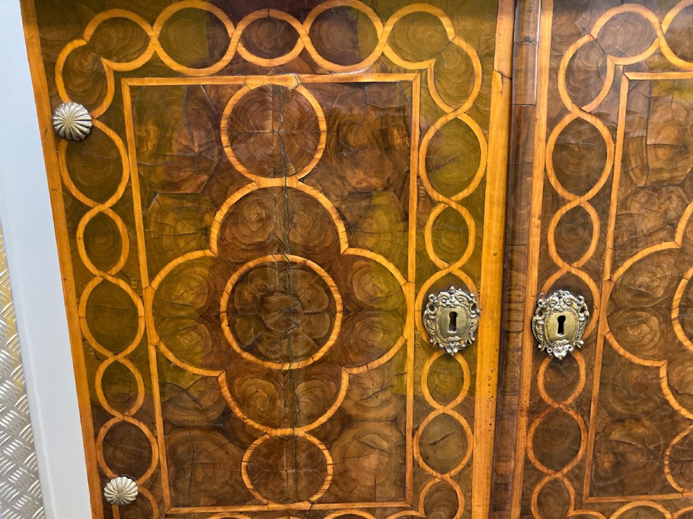 A William & Mary walnut cabinet on stand featuring door panels decorated with geometric oyster veneer stringing, resting on six barley-twist legs with a shaped stretcher base. View III