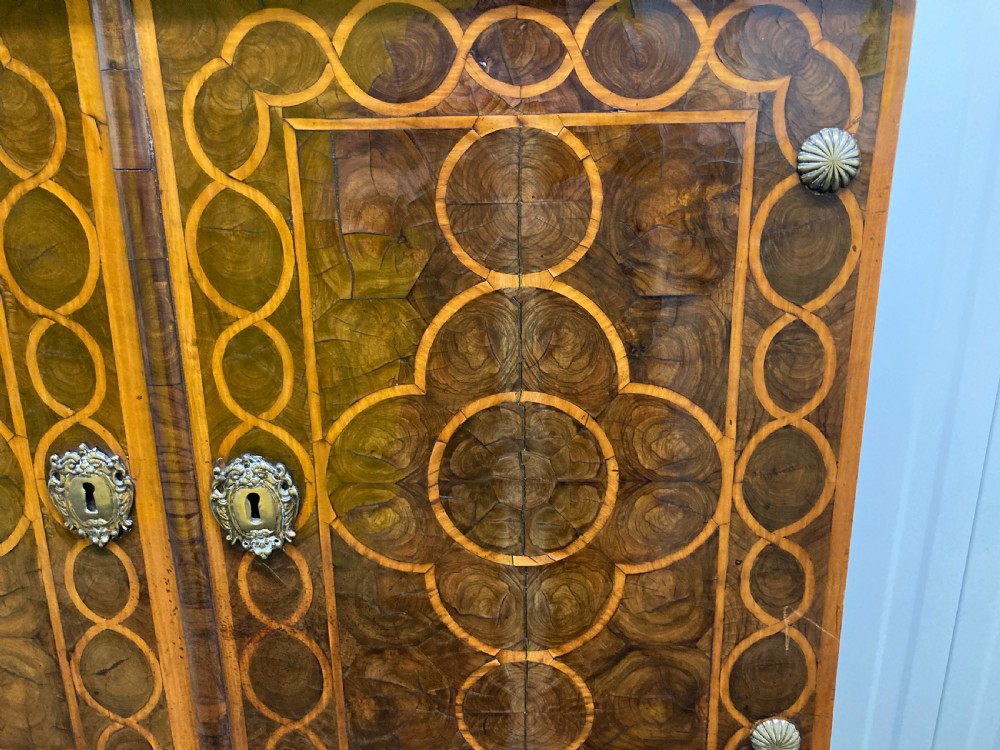 A William & Mary walnut cabinet on stand featuring door panels decorated with geometric oyster veneer stringing, resting on six barley-twist legs with a shaped stretcher base. View V