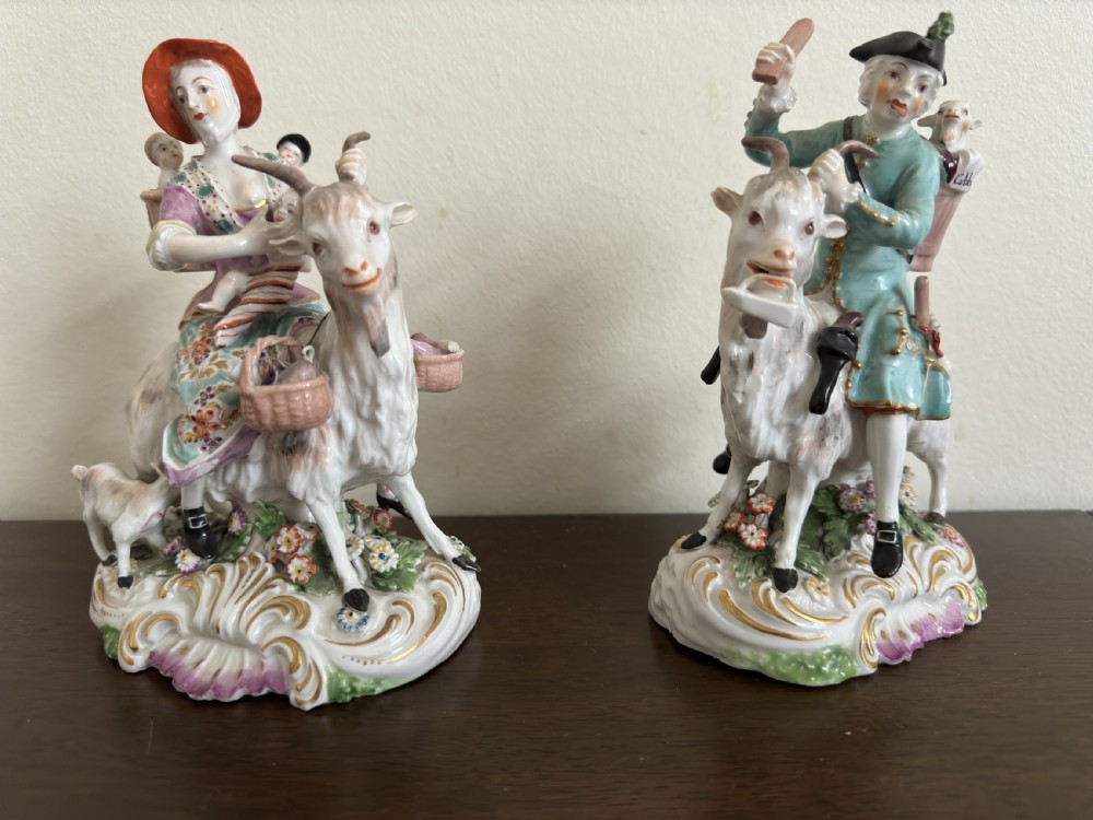 A pair of antique hand-painted porcelain figures depicting a man and woman riding goats decorated with floral details and rococo bases. View II