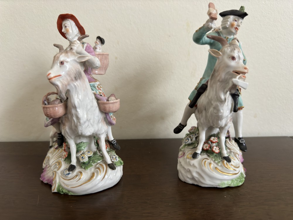 A pair of antique hand-painted porcelain figures depicting a man and woman riding goats decorated with floral details and rococo bases. View III