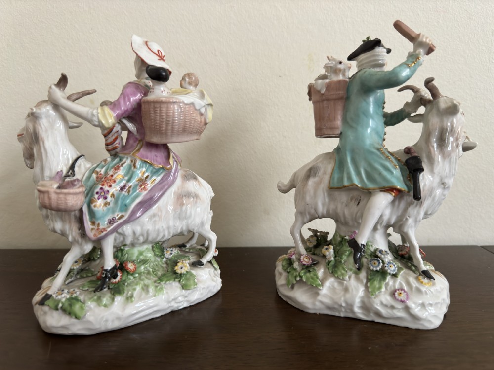 A pair of antique hand-painted porcelain figures depicting a man and woman riding goats decorated with floral details and rococo bases. View VI