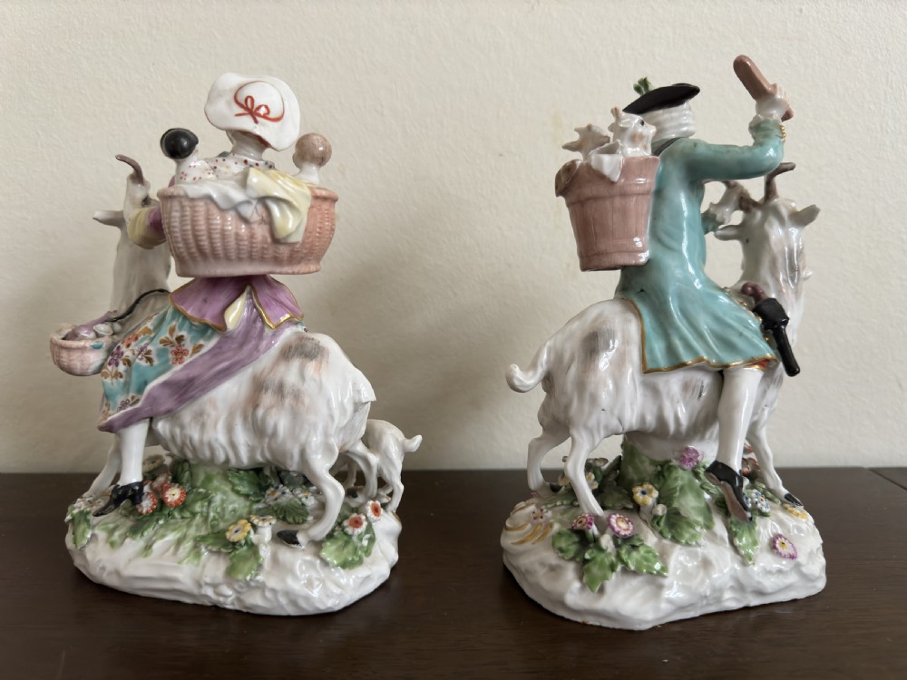 A pair of antique hand-painted porcelain figures depicting a man and woman riding goats decorated with floral details and rococo bases. View VII