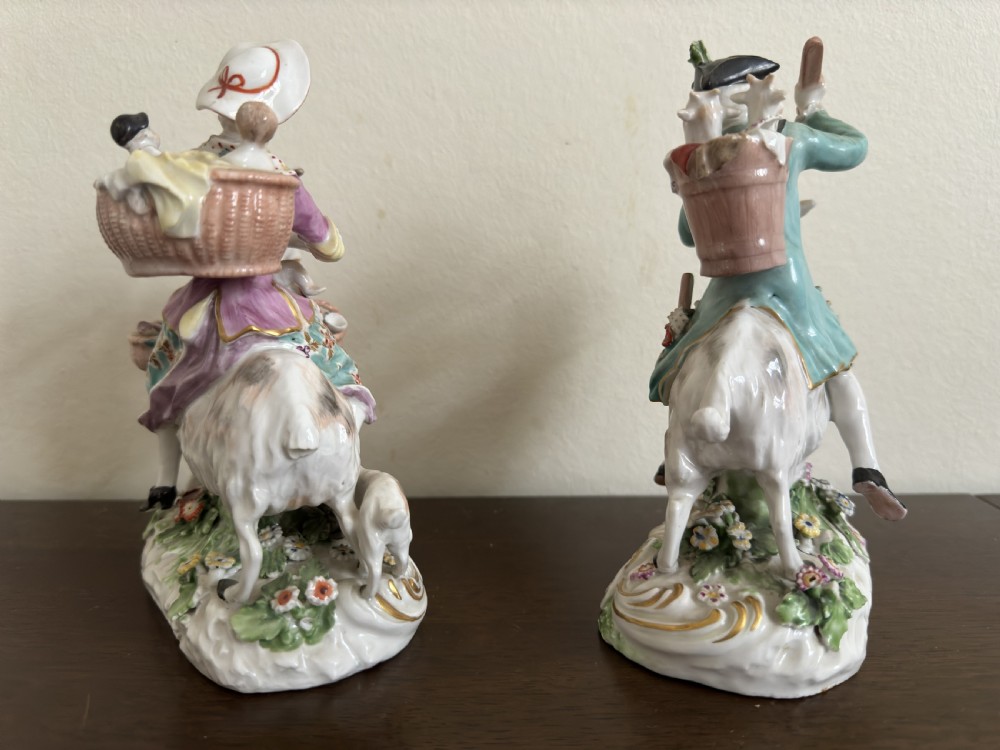 A pair of antique hand-painted porcelain figures depicting a man and woman riding goats decorated with floral details and rococo bases. View VIII