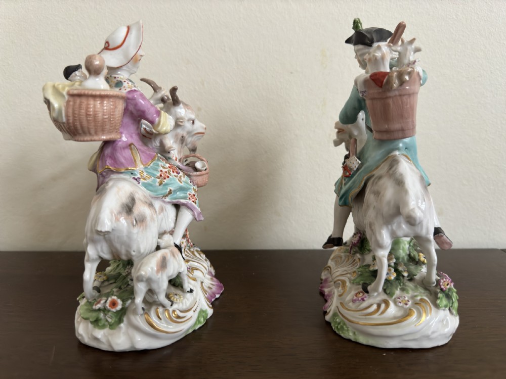 A pair of antique hand-painted porcelain figures depicting a man and woman riding goats decorated with floral details and rococo bases. View IX