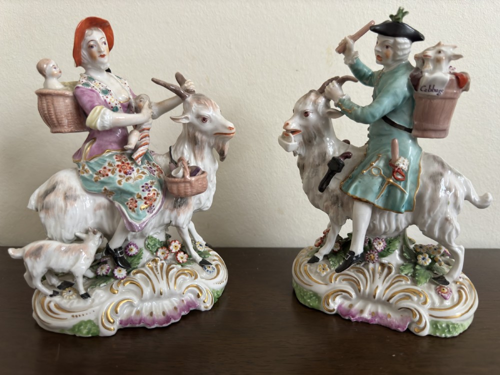 A pair of antique hand-painted porcelain figures depicting a man and woman riding goats decorated with floral details and rococo bases. View XI