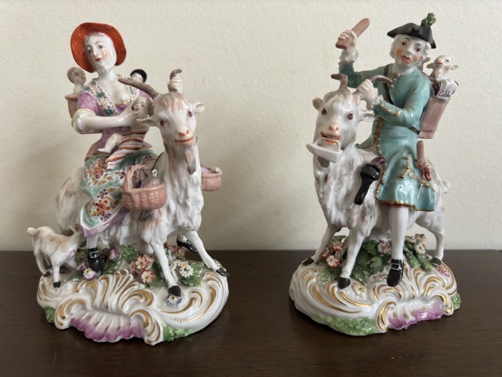 A pair of antique hand-painted porcelain figures depicting a man and woman riding goats decorated with floral details and rococo bases. View XII