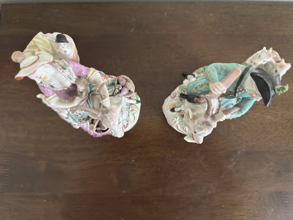 A pair of antique hand-painted porcelain figures depicting a man and woman riding goats decorated with floral details and rococo bases. View XIV