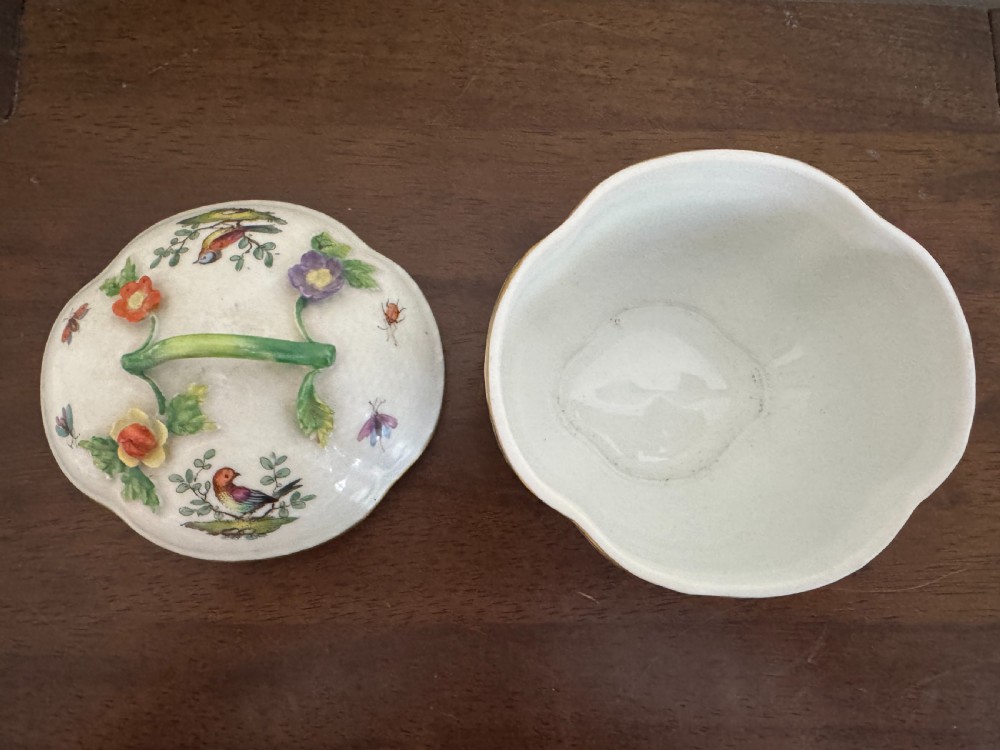 A white Dresden porcelain lidded bowl featuring relief basketweave moulding, hand-painted birds and insects, a branch handle, and gilt borders. View X