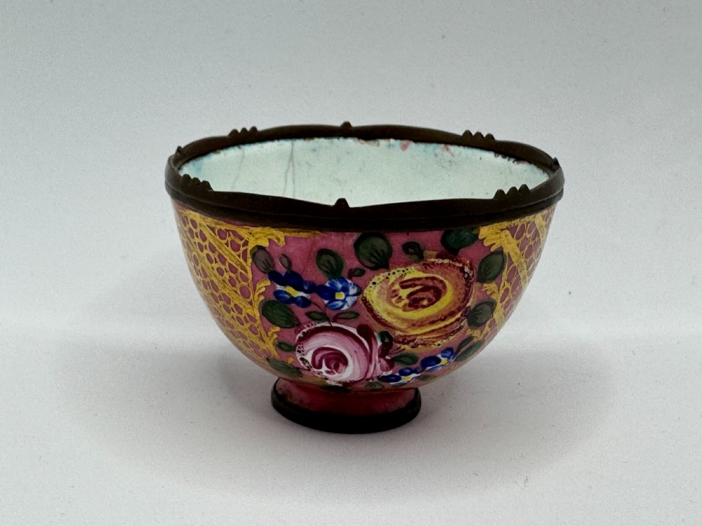 An 18th-century Limoges enamel salt bowl featuring hand-painted floral motifs on a pink ground with gilt lattice detailing and a dark metal rim.