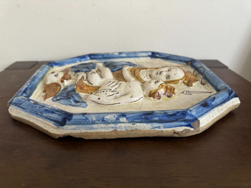 An octagonal 18th-century tin-glazed ceramic plaque depicting the Madonna holding the Christ Child in raised relief with blue and yellow accents. View IX