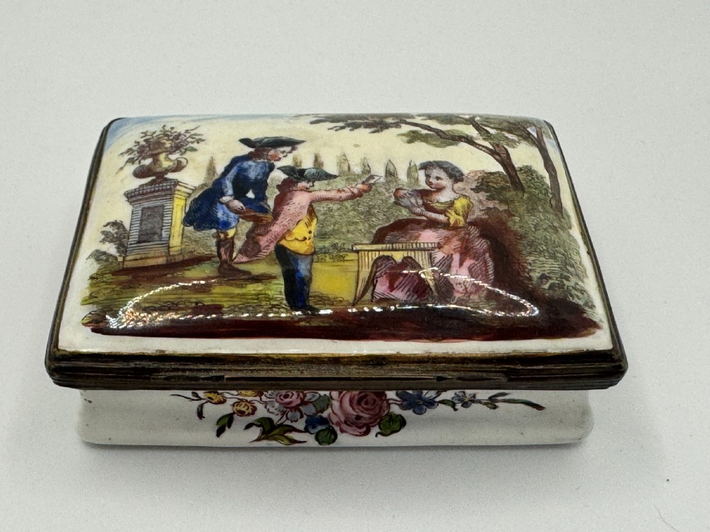 A rectangular 18th-century Bilston enamel box decorated with a painted pastoral scene on the lid and floral sprigs along the white base.