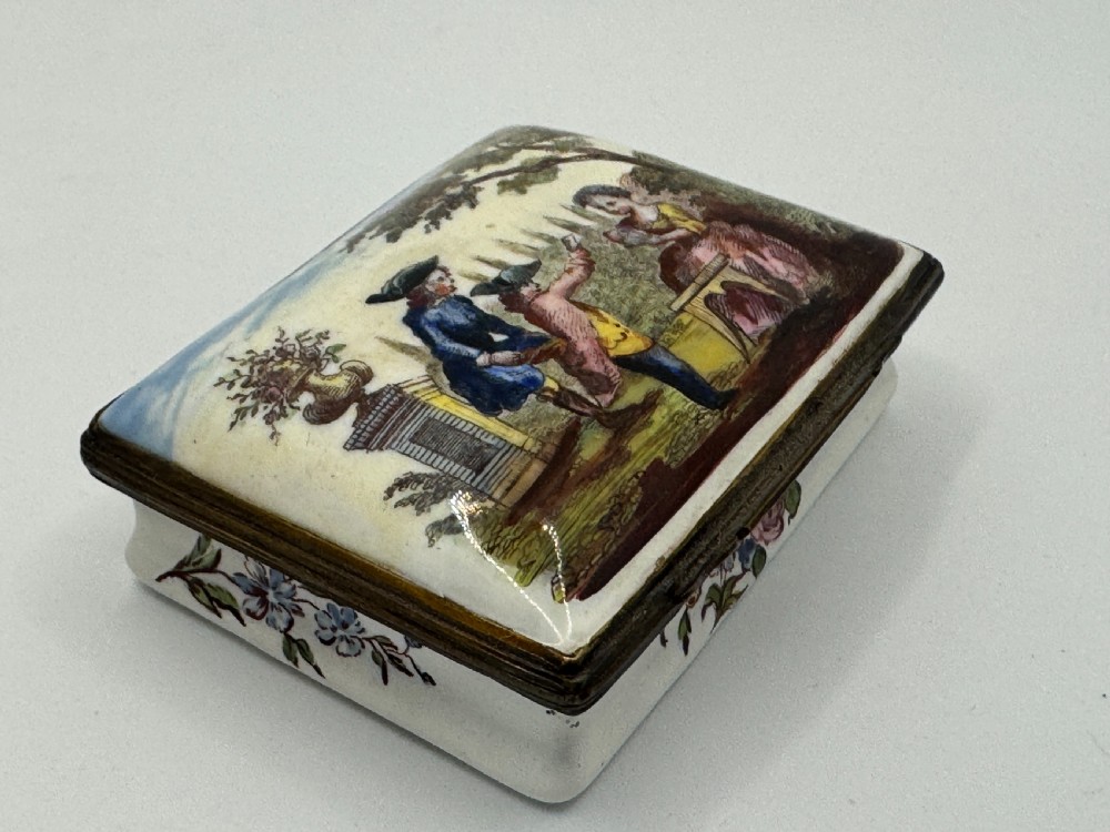 A rectangular 18th-century Bilston enamel box decorated with a painted pastoral scene on the lid and floral sprigs along the white base. View II