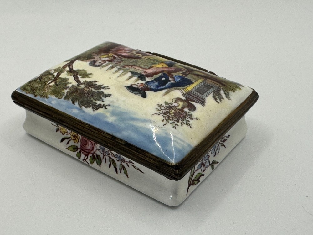 A rectangular 18th-century Bilston enamel box decorated with a painted pastoral scene on the lid and floral sprigs along the white base. View V