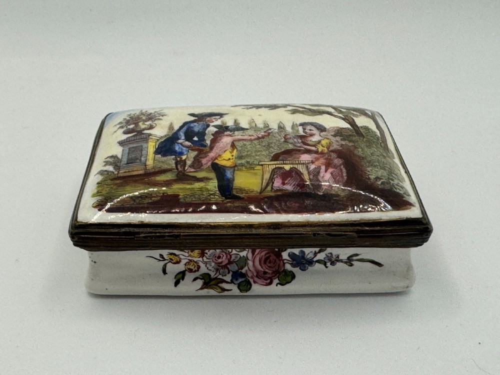 A rectangular 18th-century Bilston enamel box decorated with a painted pastoral scene on the lid and floral sprigs along the white base. View X