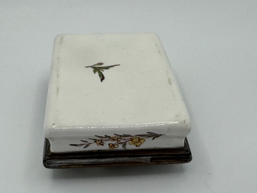 A rectangular 18th-century Bilston enamel box decorated with a painted pastoral scene on the lid and floral sprigs along the white base. View XIII