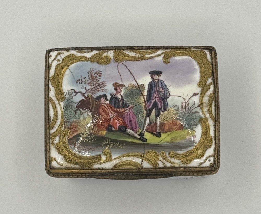 A small 19th-century rectangular enamel box decorated with a hand-painted pastoral scene surrounded by gilt scrollwork.