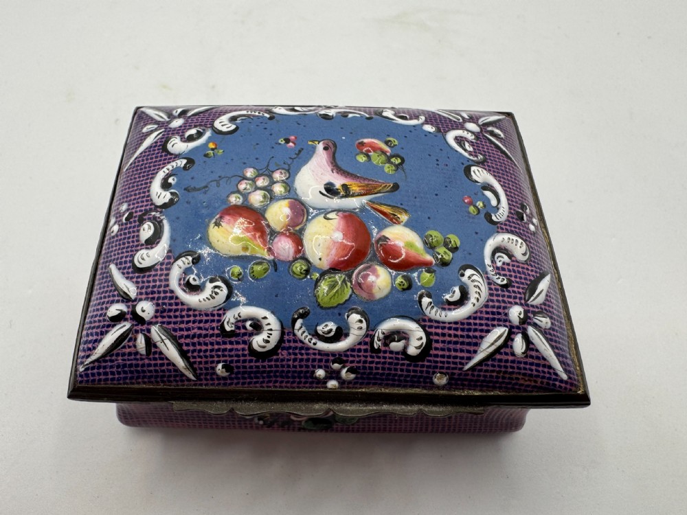 A rectangular eighteenth-century enamel box decorated with a central painted bird and fruit motif framed by white scrollwork against a purple lattice background.