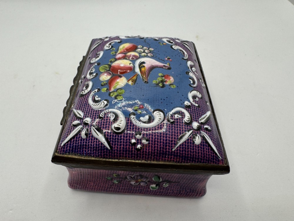 A rectangular eighteenth-century enamel box decorated with a central painted bird and fruit motif framed by white scrollwork against a purple lattice background. View II