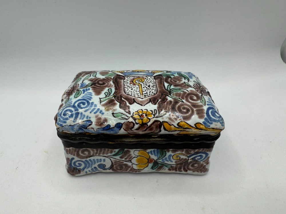 A small rectangular 17th-century Dutch Delft tin-glazed earthenware box featuring hand-painted polychrome floral motifs and an armorial shield crest.