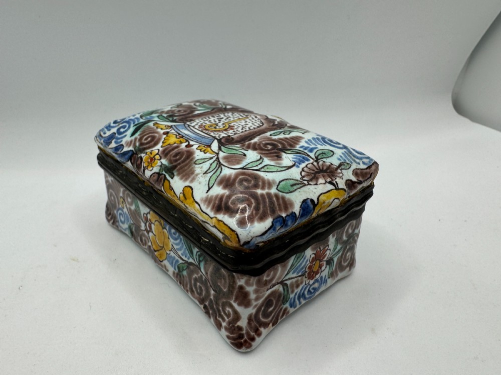 A small rectangular 17th-century Dutch Delft tin-glazed earthenware box featuring hand-painted polychrome floral motifs and an armorial shield crest. View V