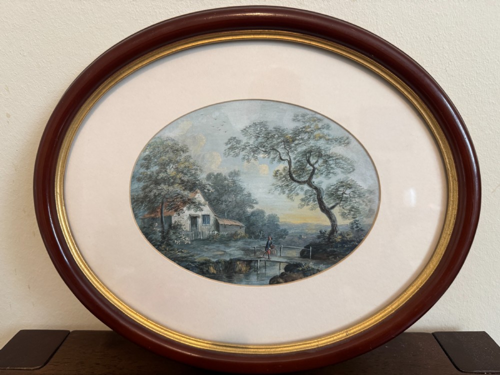 An oval 19th-century watercolour painting depicting a figure and dog crossing a stone bridge over a river, presented in a dark wood frame with a gold slip. View V