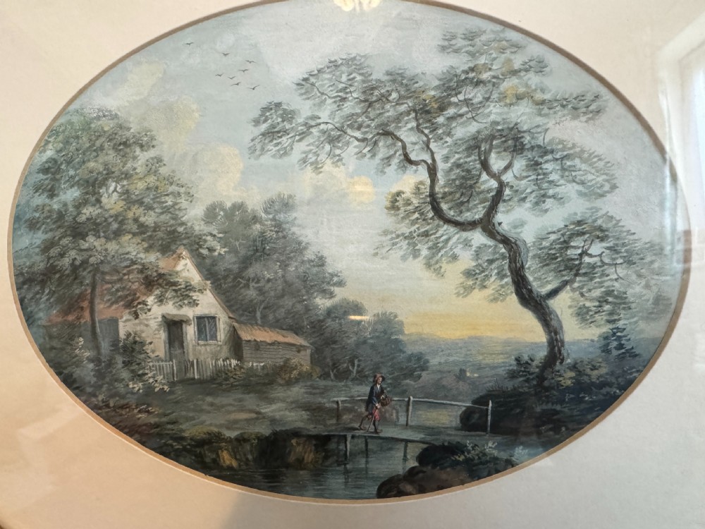 An oval 19th-century watercolour painting depicting a figure and dog crossing a stone bridge over a river, presented in a dark wood frame with a gold slip. View VI