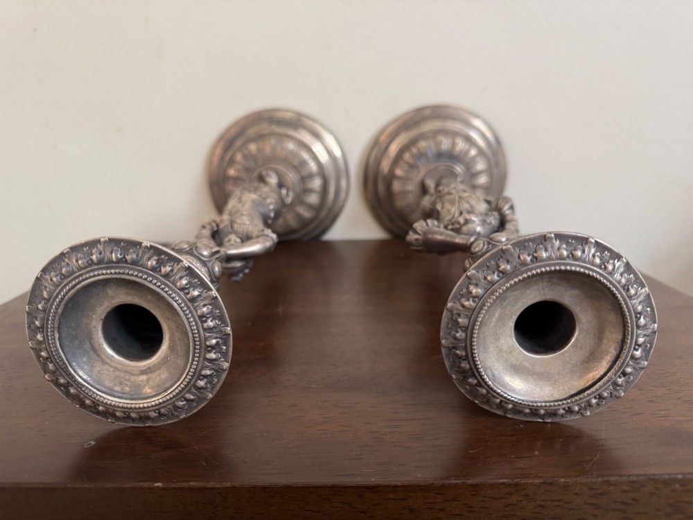 A pair of antique silver-plated candlesticks featuring detailed sculpted figures of a lady and a cavalier supporting sconces on rounded bases. View X