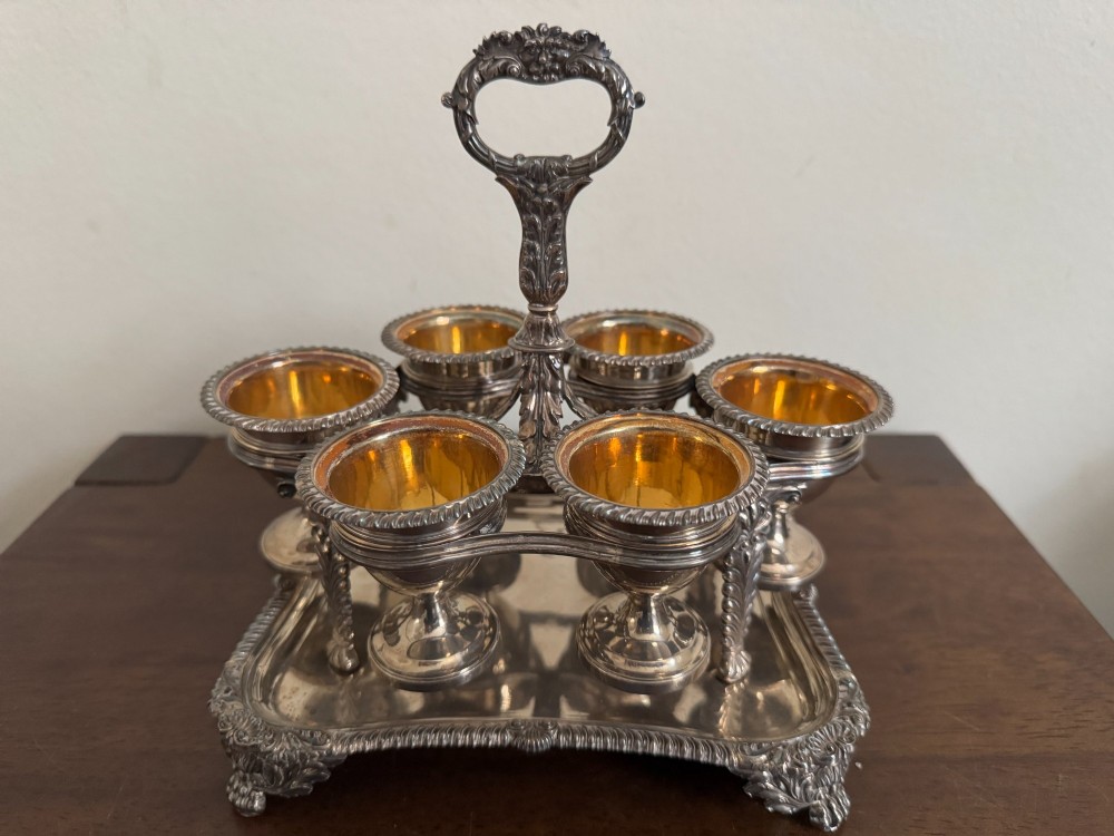 A Georgian sterling silver egg cruet stand holding six gilt-lined silver egg cups on a raised tray base with a central handle.