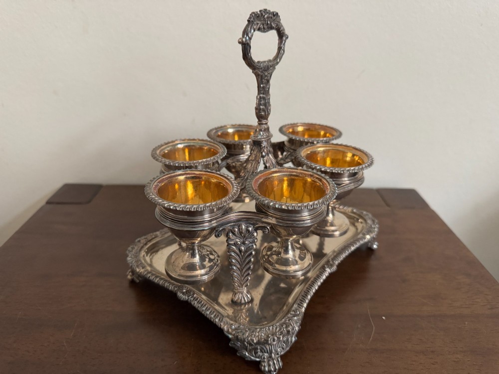 A Georgian sterling silver egg cruet stand holding six gilt-lined silver egg cups on a raised tray base with a central handle. View II