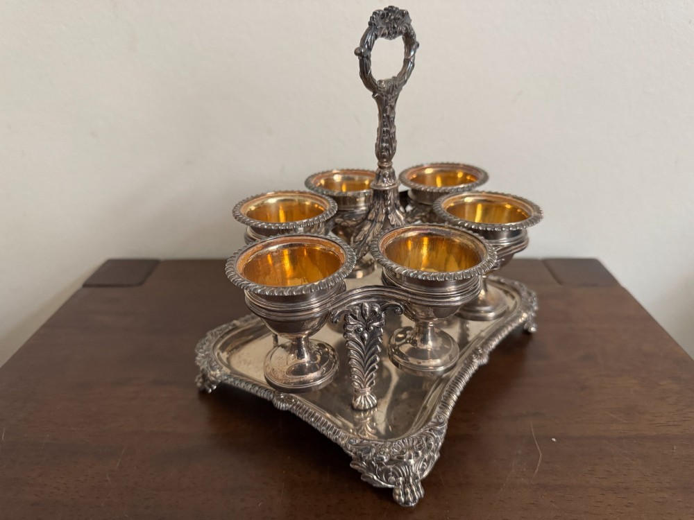 A Georgian sterling silver egg cruet stand holding six gilt-lined silver egg cups on a raised tray base with a central handle. View IV