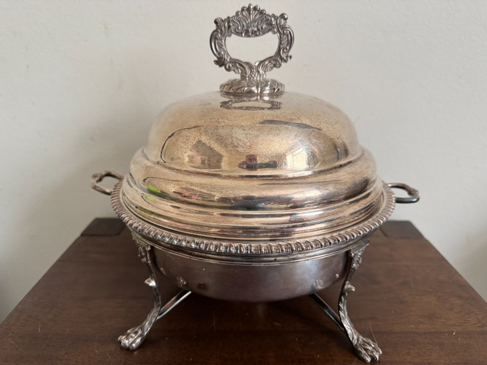 A George III sterling silver domed supper dish featuring cast handles, gadrooned borders, and a matching stand supported by paw feet.