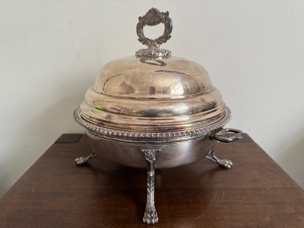 A George III sterling silver domed supper dish featuring cast handles, gadrooned borders, and a matching stand supported by paw feet. View II