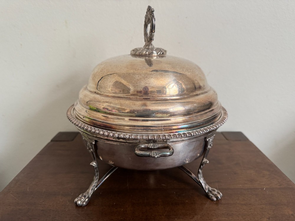 A George III sterling silver domed supper dish featuring cast handles, gadrooned borders, and a matching stand supported by paw feet. View III