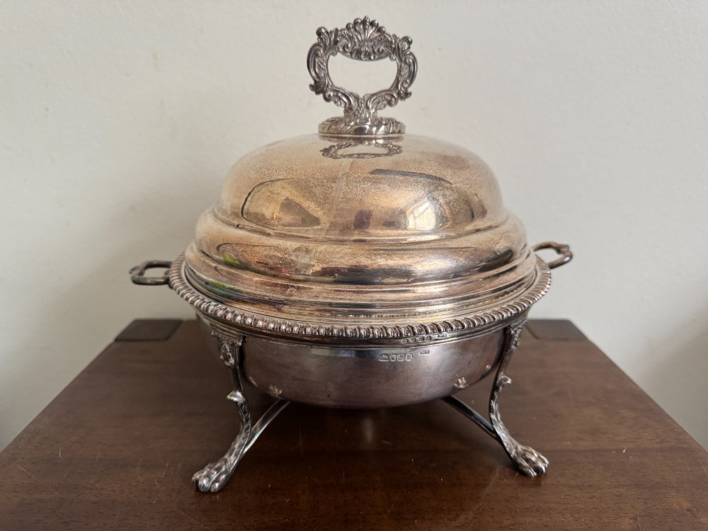 A George III sterling silver domed supper dish featuring cast handles, gadrooned borders, and a matching stand supported by paw feet. View V