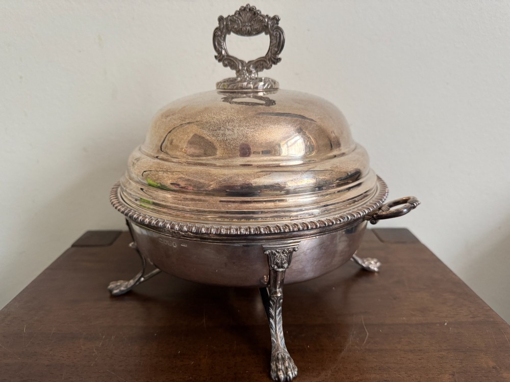 A George III sterling silver domed supper dish featuring cast handles, gadrooned borders, and a matching stand supported by paw feet. View VI