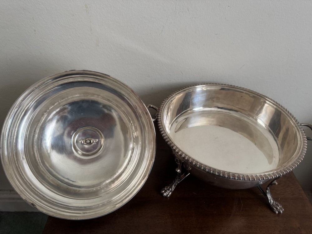 A George III sterling silver domed supper dish featuring cast handles, gadrooned borders, and a matching stand supported by paw feet. View X