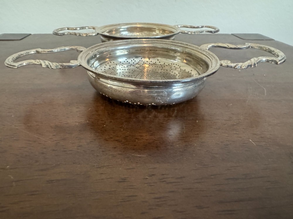 A matched pair of George III sterling silver lemon strainers featuring pierced geometric bowl patterns and dual side handles. View III